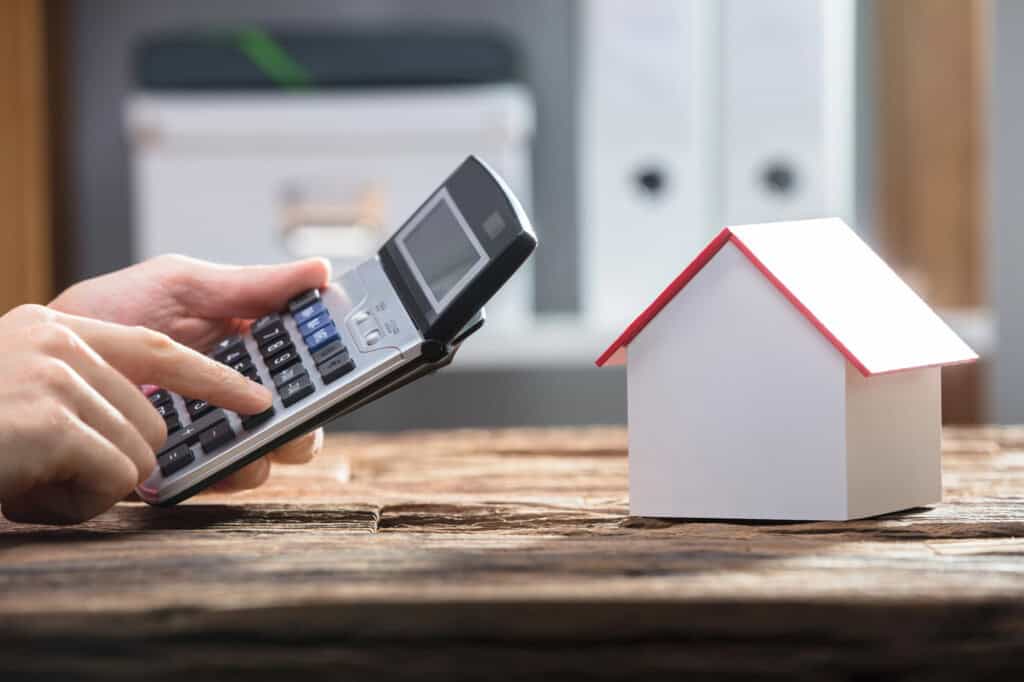 A photo of a man's hands using a calculator and a small wooden house