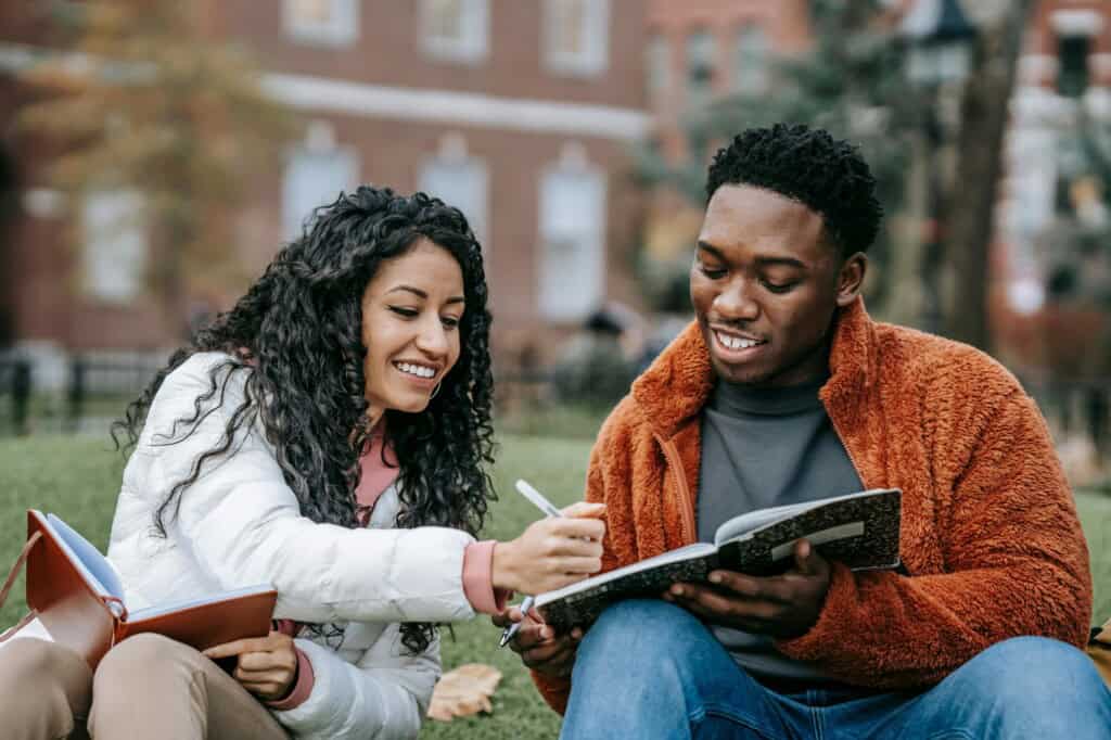 College students holding their notebooks while sitting on the school grounds