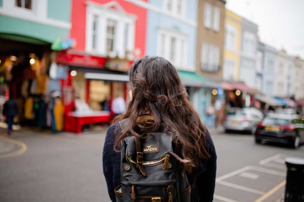 Picture of a woman with a backpack and long hair standing in front of a blurry neighbourhood from London