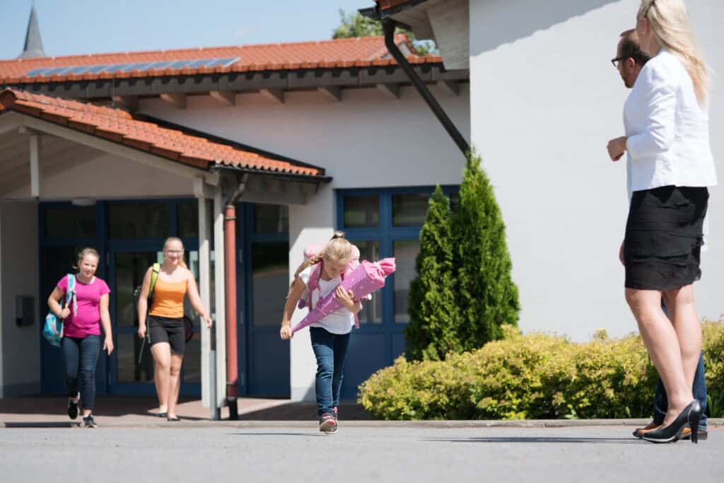 A young female student is running toward her parents after her first day at school.