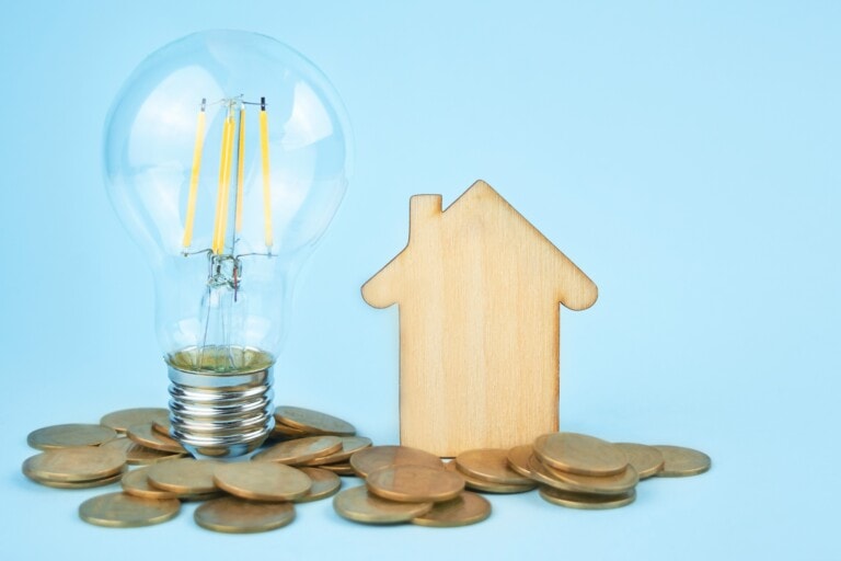 A wooden house with a light bulb and coins in the concept of 'how to save money when moving to Bromley'.