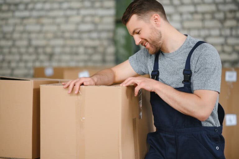 A smiling professional packer surrounded by cartons in the concept of 'Benefits of Hiring Professional Packers for Office Removals'.